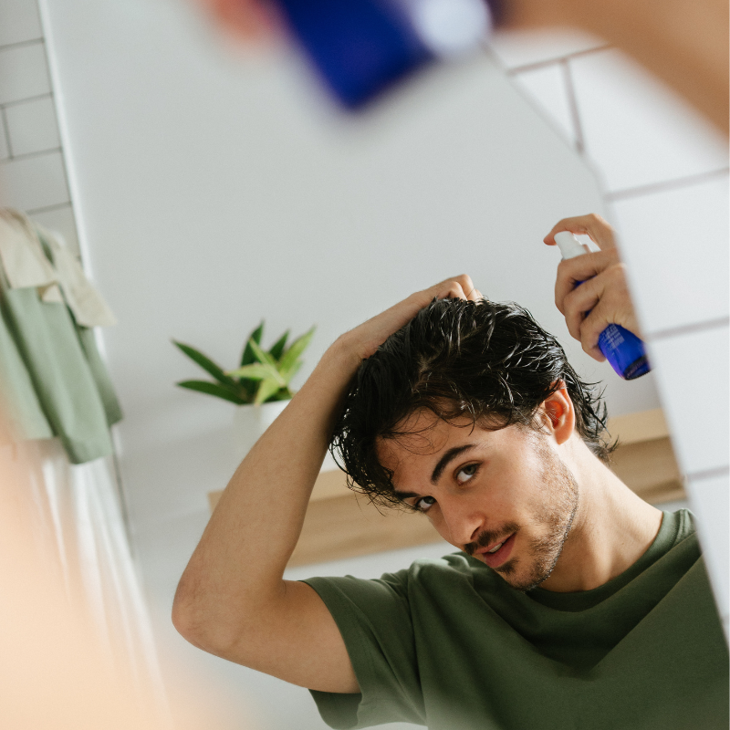 Man applying Salty Hair sea salt spray while looking into bathroom mirror